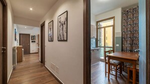 A hallway with wooden flooring, a dining area with a wooden table and chairs, and a kitchen visible through an open door. - GuestHost - Garbatella Apartment - Roma (Roma)