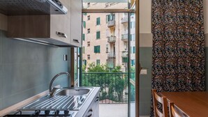 A compact kitchen with a gas stove, a sink, and a view of a balcony with a railing. - GuestHost - Garbatella Apartment - Roma (Roma)