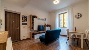 A modern living room with a sofa, TV, wooden flooring, and a dining area with chairs and a table. - GuestHost - Garbatella Apartment - Roma (Roma)