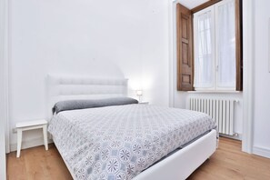 A bedroom with a bed, a nightstand, a window with curtains, and a radiator.