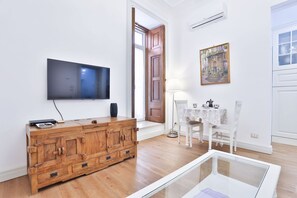 A living room with a wooden cabinet, a flat-screen TV, a white table with chairs, and a painting on the wall.