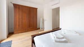 A bedroom with a wooden wardrobe, a bed with white linens, and a modern light fixture. - GuestHost - Cozy apartment near Trotter Park (Milano)