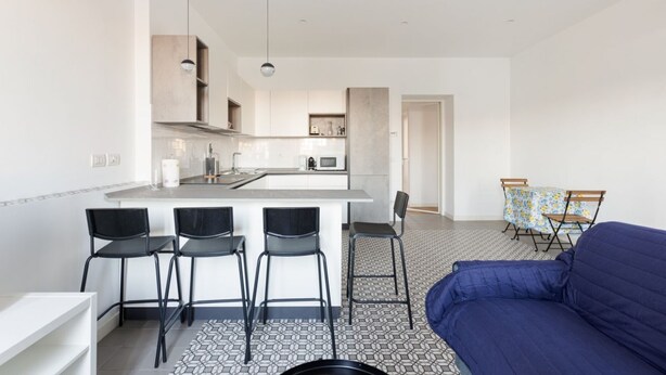 A modern kitchen with a central island, bar stools, and a blue sofa in a living area. - GuestHost - Cozy apartment near Trotter Park (Milano)