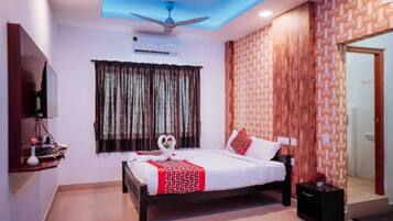 A hotel room with a bed, a ceiling fan, an air conditioning unit, a mirror, and a patterned wall.