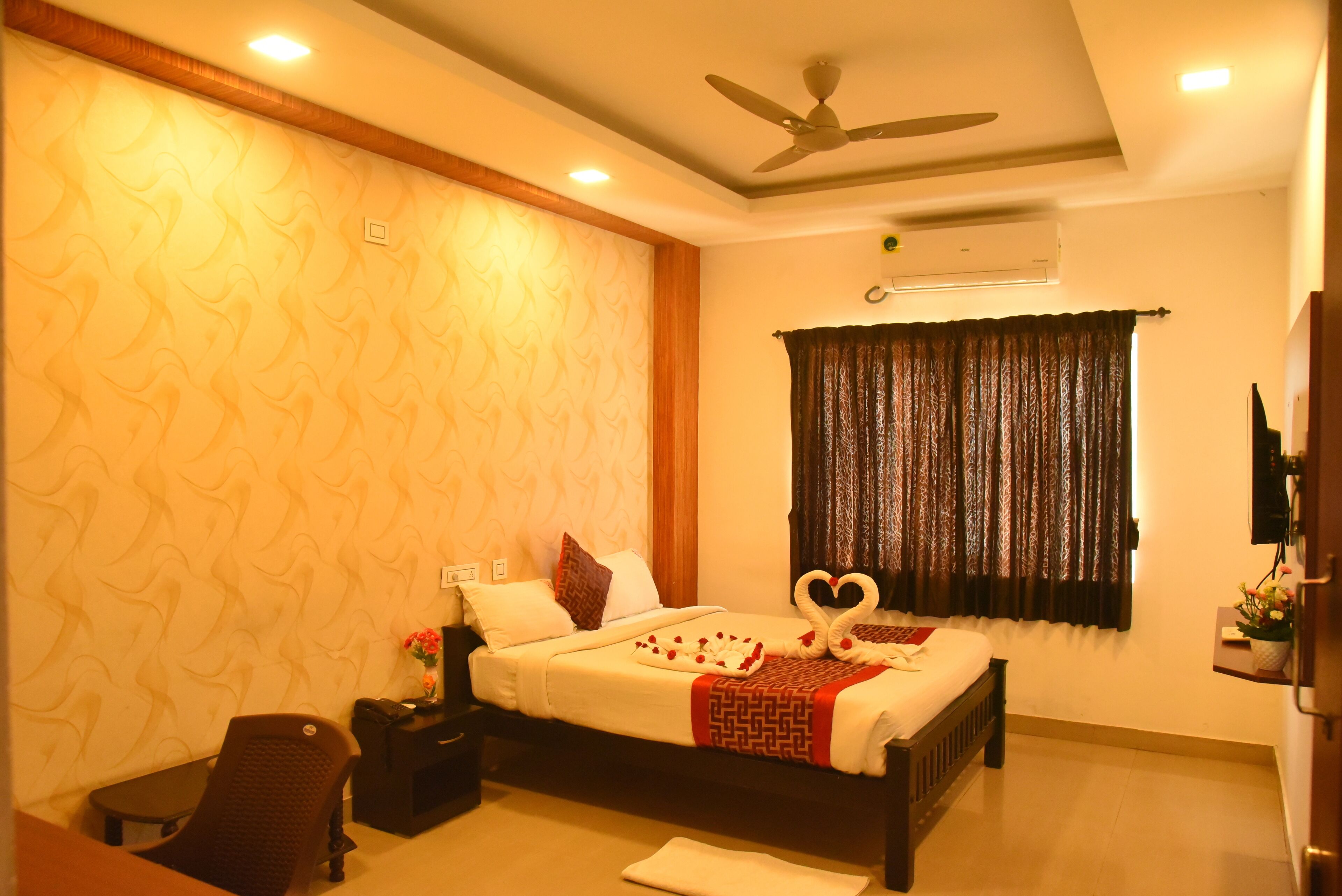 A neatly arranged hotel room with a bed, a desk, a chair, a ceiling fan, and a window with curtains.