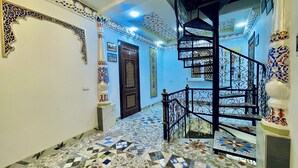 A hallway with a tiled floor, a wooden door, and a spiral staircase with ornate railings. - SHOM EAST HOTEL (Bukhara)