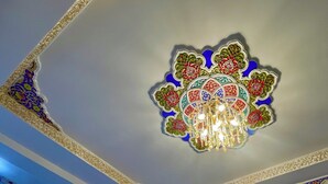A ceiling with intricate floral and geometric patterns, a chandelier, and a decorative border. - SHOM EAST HOTEL (Bukhara)