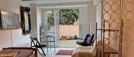 A room with a bed, a desk, a chair, a table, and a large window.