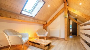 A loft-style room with wooden beams, a skylight, two upholstered chairs, a wooden coffee table, and a radiator.