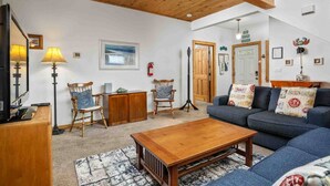 A cozy living room with a wooden ceiling, a blue sofa, a wooden coffee table, and two rocking chairs. - Charming Beach Hideaway w/ Fire Pit, Deck, & Close to Beach, Shops, Restaurants,and Sunset Views (Rockaway Beach)