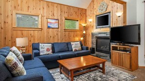 A cozy living room with a wooden wall, a fireplace, a sofa, a coffee table, and a TV. - Charming Beach Hideaway w/ Fire Pit, Deck, & Close to Beach, Shops, Restaurants,and Sunset Views (Rockaway Beach)