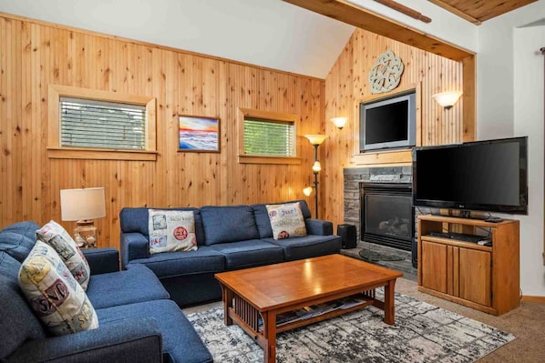 A cozy living room with a wooden wall, a fireplace, a sofa, a coffee table, and a TV. - Charming Beach Hideaway w/ Fire Pit, Deck, & Close to Beach, Shops, Restaurants,and Sunset Views (Rockaway Beach)