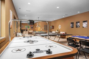 Une pièce équipée d’un baby-foot, d’une table de billard et d’une table de snooker. On y trouve des chaises et une table, avec une table de billard en arrière-plan.