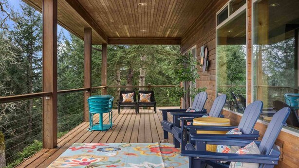 Una terraza techada con suelo de madera, mobiliario exterior y grandes ventanales que ofrecen vistas del bosque circundante.