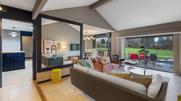 A modern living room with a large mirror, a sofa, and a dining area with outdoor seating. - Incredible Golfside Single Level Ranch, Open Layout w/ Vintage Charm, Huge Patio, Close 2 Everything (Gresham)