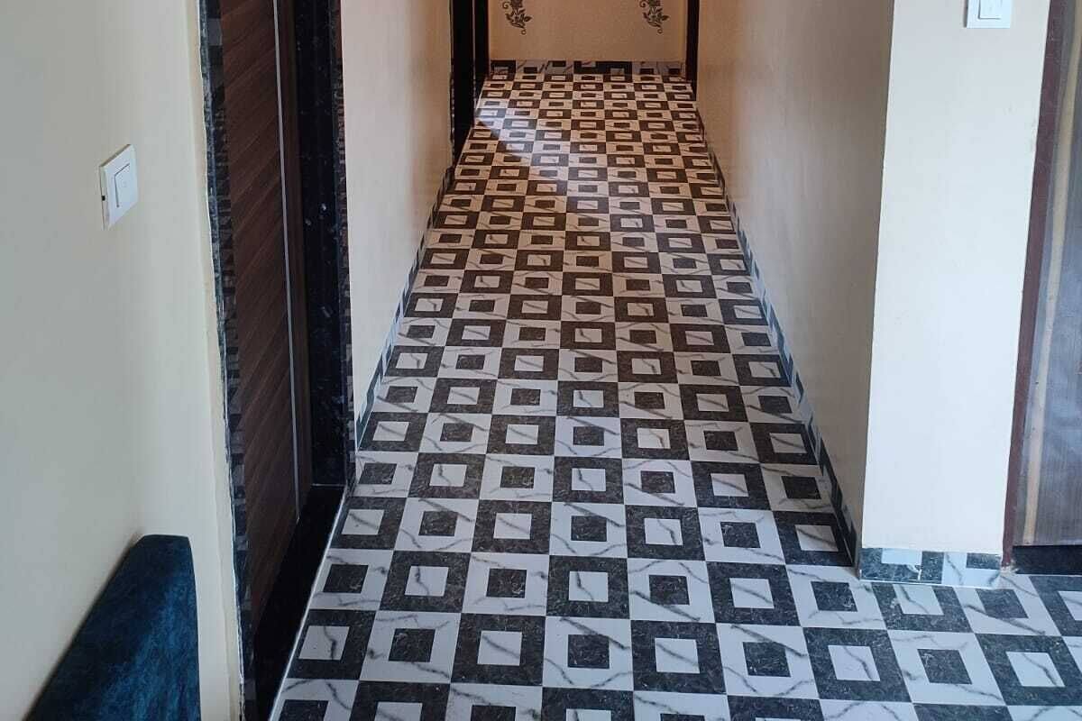 Un couloir étroit, dont le sol est recouvert de carreaux décoratifs, avec deux appliques murales et une porte sur le côté gauche.
