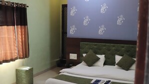Un dormitorio con una cama, un ventilador de techo, un papel tapiz estampado y un taburete verde pequeño.