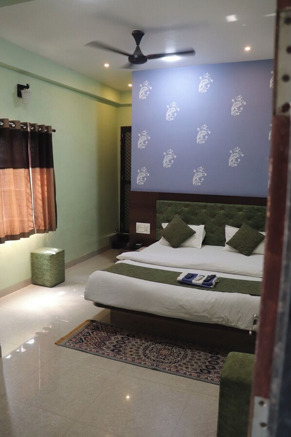 A bedroom with a bed, a ceiling fan, a patterned wall, and a small green stool. - Hotel Shivalay Palace (Maheshwar)