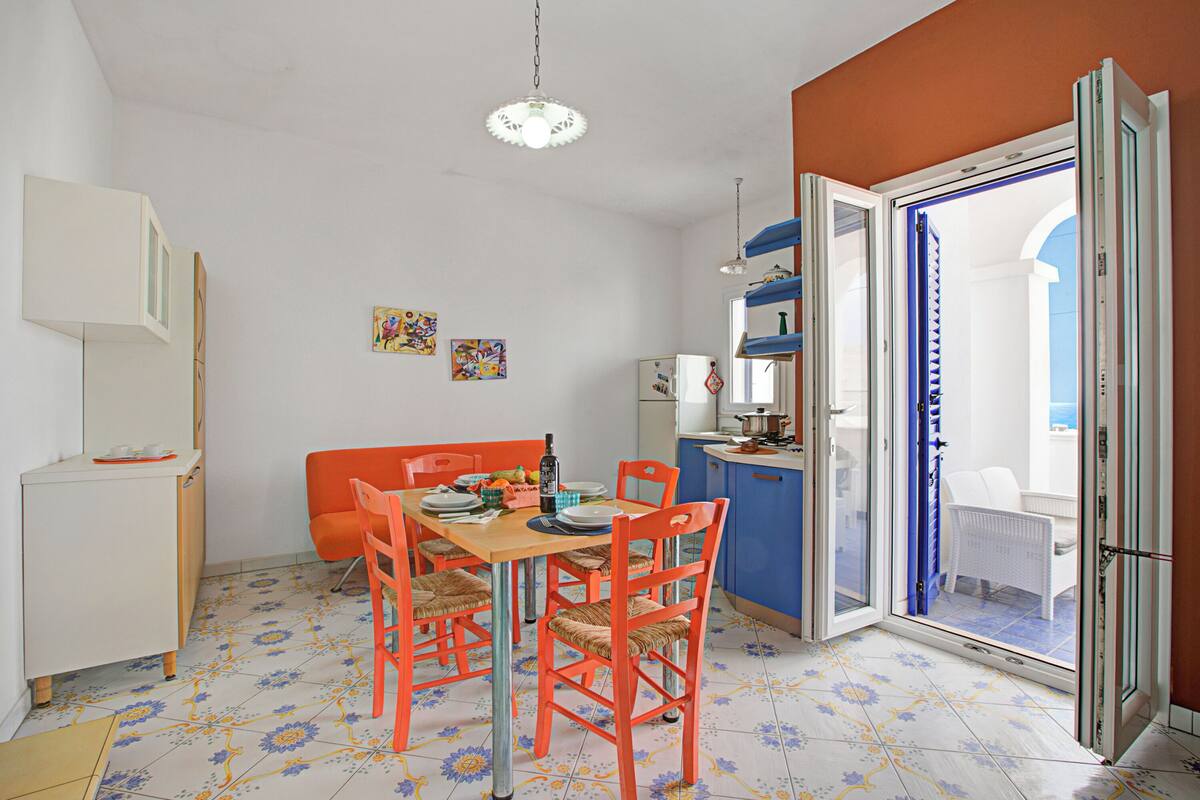 A dining area with a table and chairs, a kitchen area with a refrigerator, and a sliding glass door leading to a balcony.