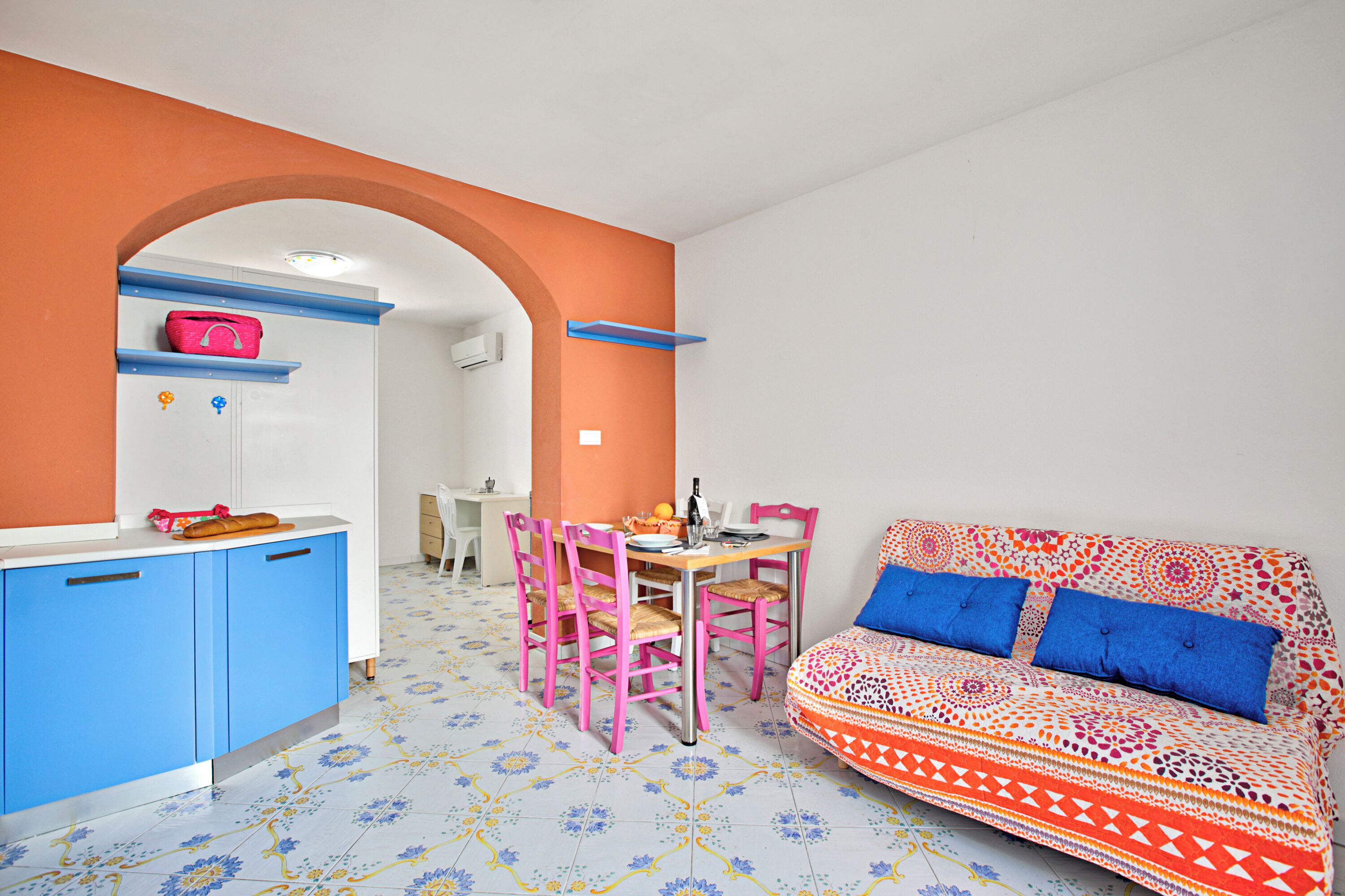 Una habitación con kitchenette, un comedor con sillas y una mesa, y un sofá con cojines estampados.