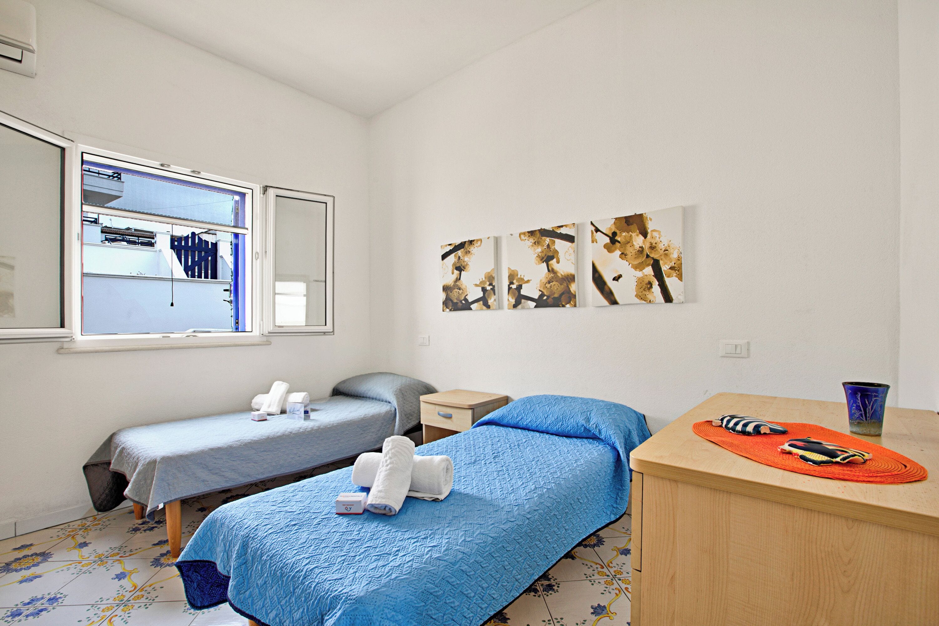 Une chambre avec deux lits, une petite table, un miroir et des œuvres d’art accrochées au mur.