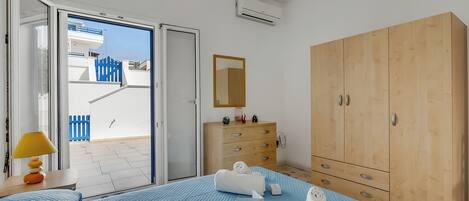 A hotel room with a bed, a wooden wardrobe, a bedside table with a lamp, and a view of the outside balcony.