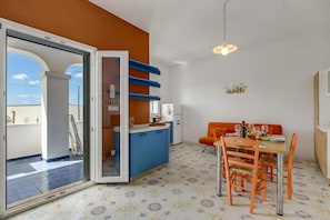 A kitchen with blue cabinets, a dining area with orange chairs, and a view through a glass door. - Complesso Azzurro Apartments (Morciano di Leuca)