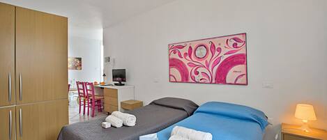 Een hotelkamer met twee bedden, een bureau, een stoel, een kledingkast en een schilderij aan de muur.