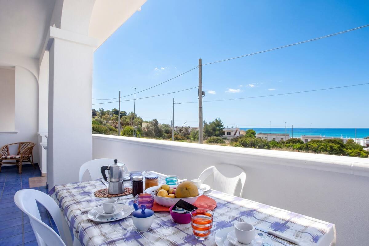 A balcony with a table set for breakfast, overlooking a coastal view.