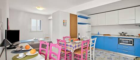 A compact kitchen with white cabinets, a blue countertop, and a dining area with pink chairs and a table set for two.
