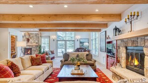 A spacious living room with a fireplace, wooden beams, and a large window. - Indoor Pool, Gym & Hot Tub Near Keystone | Crown Jewel of Keystone by AvantStay (Keystone)