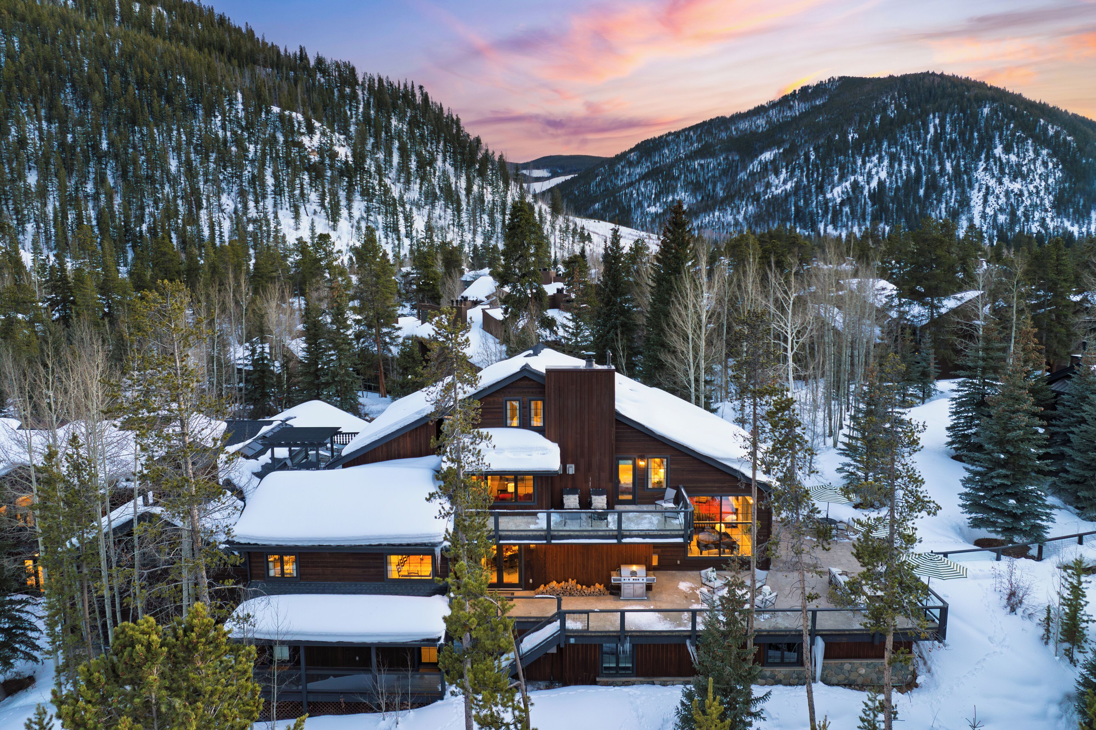 A large wooden cabin with multiple levels, surrounded by snow-covered trees and mountains.