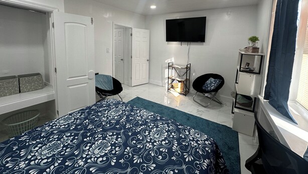 A bedroom with a bed, a TV, a chair, a desk, and a wardrobe.