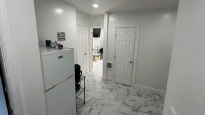 A hallway with white walls and a marble floor, leading to a door with a vent.