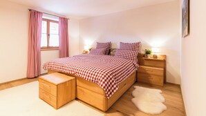 Une chambre avec un lit en bois, une literie à carreaux, une table de chevet avec une lampe, une petite commode en bois et un tapis moelleux.
