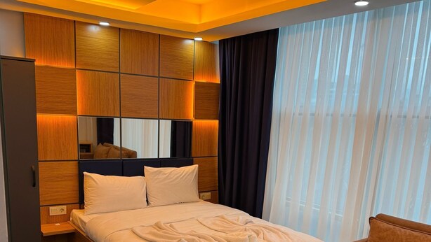 Een moderne hotelkamer met een groot bed, een houten hoofdeinde, een houten nachtkastje, een houten salontafel en een bruine bank.