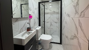 Een moderne badkamer met een marmeren spatwand, een wit wastafelmeubel, een toilet en een douchecabine met glazen wanden.