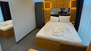 Een moderne hotelkamer met een groot bed, een houten hoofdbord, een klein zithoekje en een inbouwkast.
