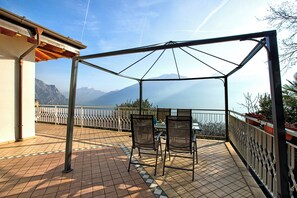 Un patio al aire libre con una mesa y sillas, vistas a montañas y una barandilla.