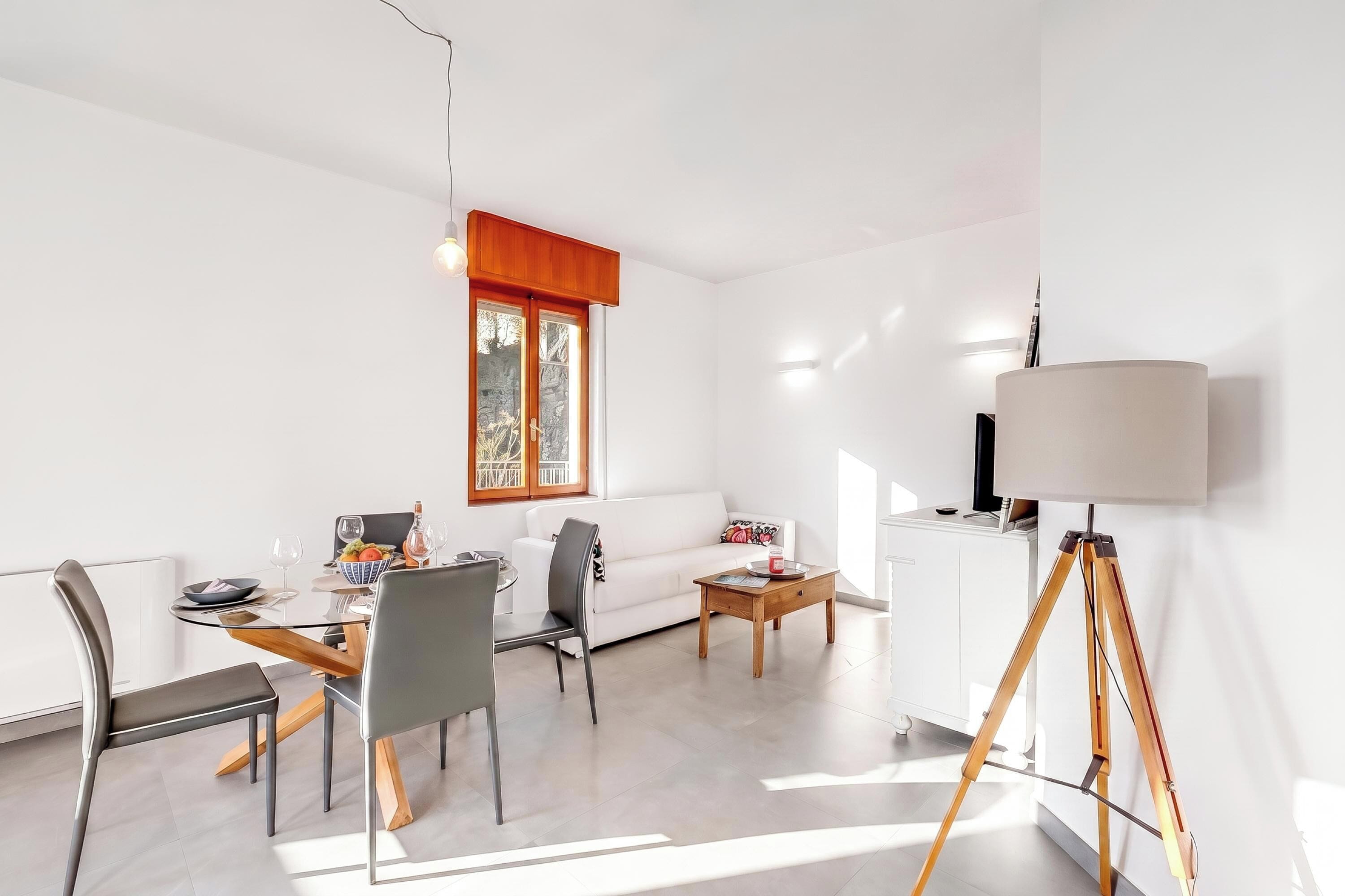 A modern living room with a dining area, white walls, and a large window.