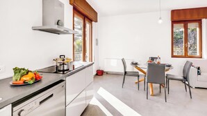 Une cuisine moderne dotée d’une cuisinière intégrée, d’un coin repas avec une table et des chaises, et de grandes fenêtres laissant entrer la lumière naturelle.