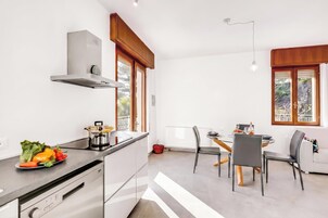 Una cucina moderna con piano cottura integrato, un'area pranzo con tavolo e sedie, e ampie finestre che offrono luce naturale.