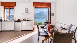 Une cuisine moderne avec vue sur les montagnes, un coin repas avec une table dressée pour deux personnes et une grande fenêtre.