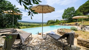 A poolside area with stone flooring, lounge chairs, and umbrellas, overlooking a scenic landscape. - In The Heart Of Chianti, Pool, Wifi, View (Lilliano)