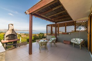 A covered patio with a stone oven, two wicker chairs, and a view of the sea. - Casa Lentischio in Stintino (Stintino)
