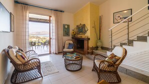 A living room with wicker furniture, a fireplace, and a view through a glass door. - Casa Lentischio in Stintino (Stintino)