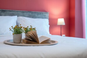 Un letto rifatto con lenzuola bianche, una lampada sul comodino e un vassoio con un libro e una pianta in vaso.