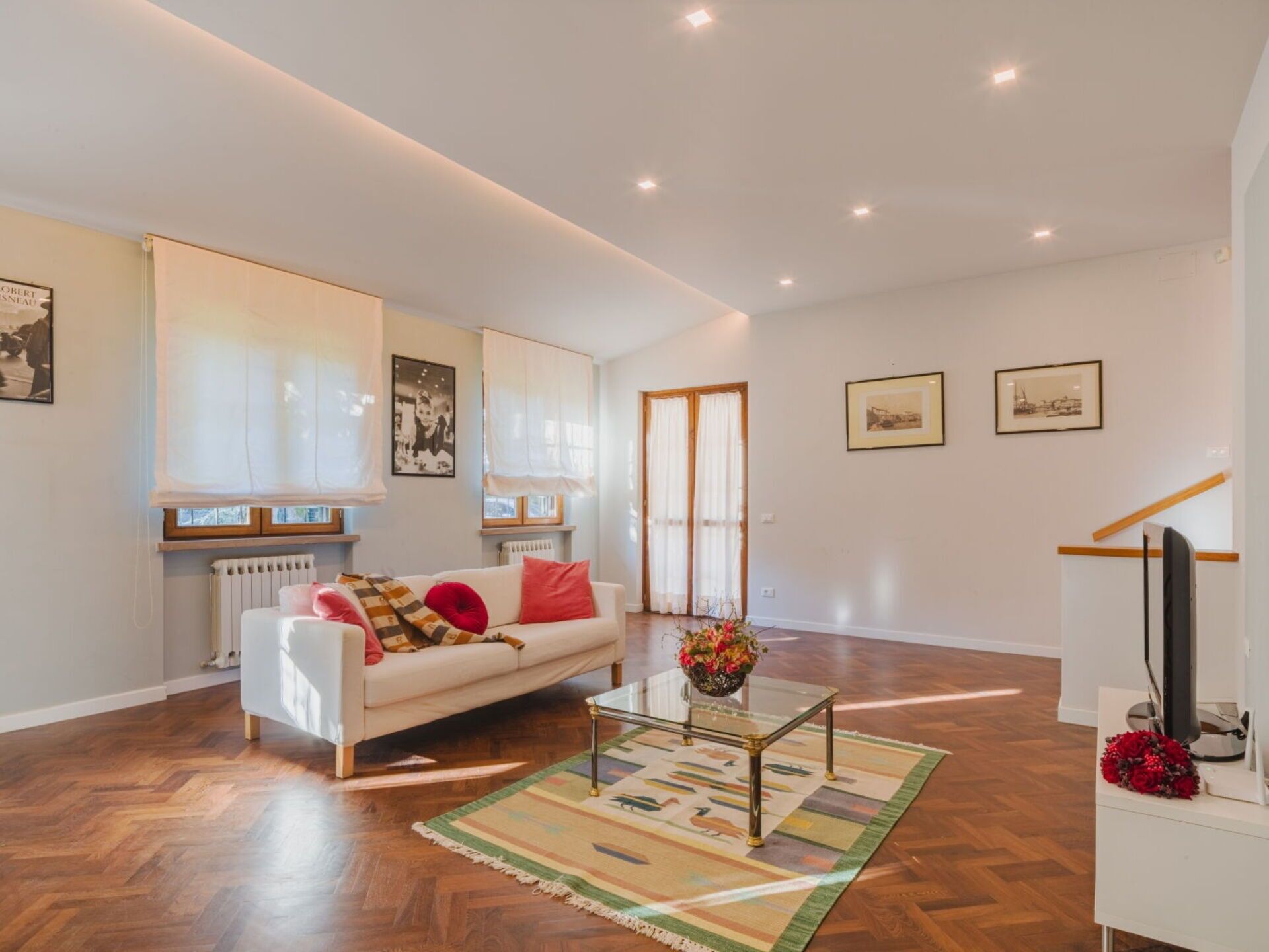 Een ruime woonkamer met een witte bank, een glazen salontafel en een houten vloer.