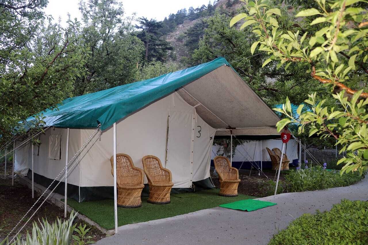 A tent with a green roof, number 3, and three wicker chairs in front.