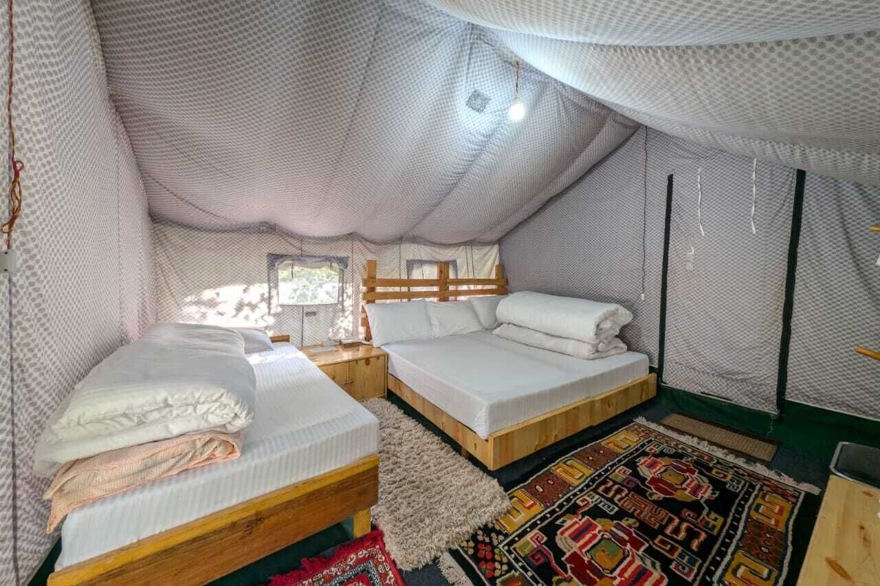 A cozy, enclosed tent-style room with two beds, a wooden headboard, a small table, and a colorful rug.